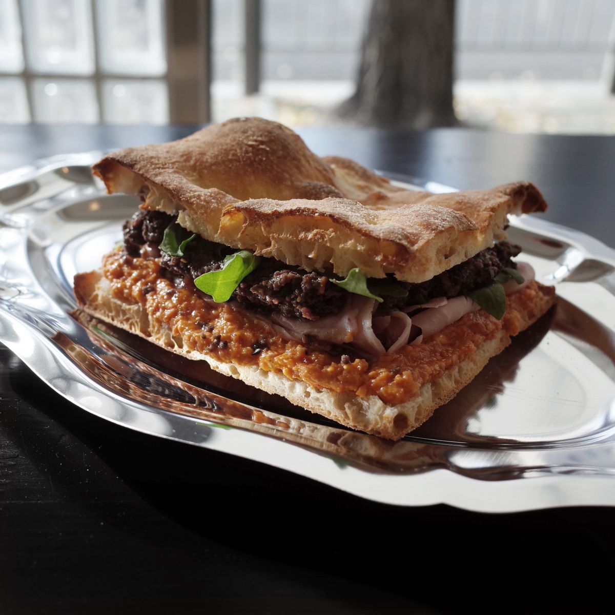 대표 메뉴 중 하나인 ‘레드 페스토 올리브 잠봉’은 매장에서 직접 구운 스키아차타 빵 사이에 토마토와 칠리 페스토, 블랙 올리브 타프나드, 잠봉, 루꼴라를 넣은 샌드위치다. / 이미지 출처: 토스티드 클럽 네이버지도 업체 제공 이미지