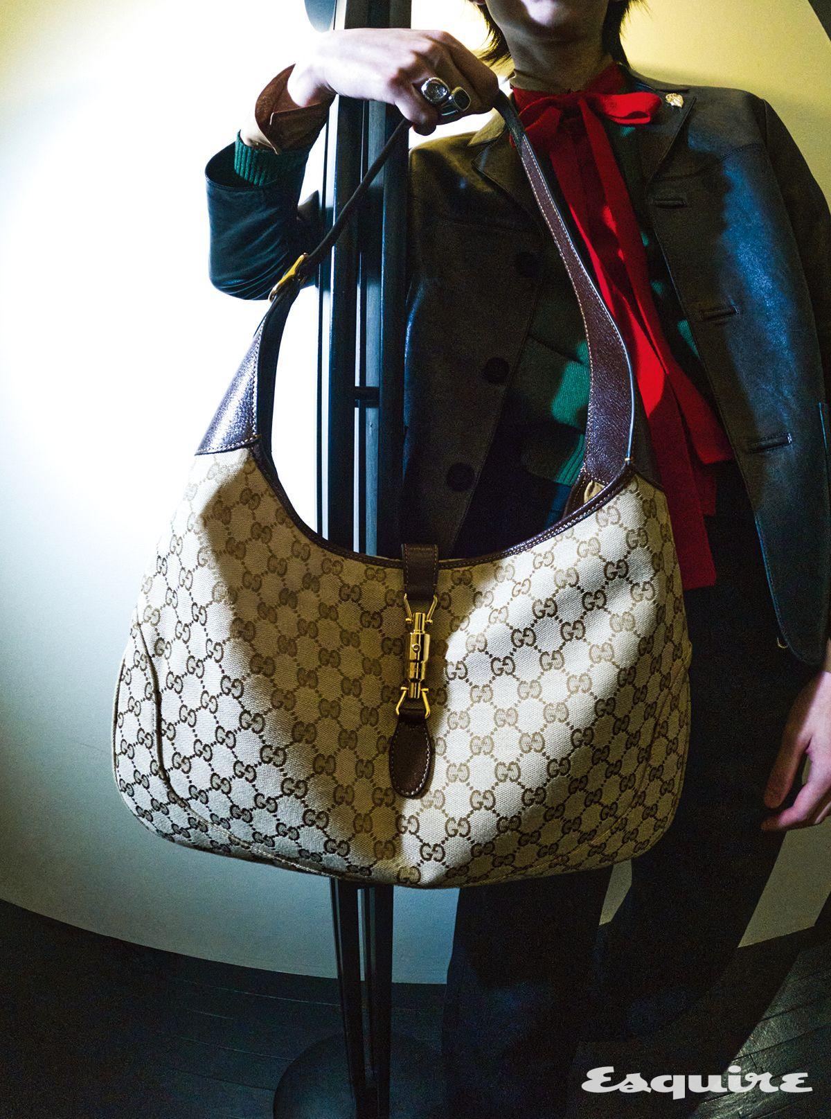 구찌 크레스트 브로치 디테일의 나파 레더 재킷, 리본 디테일의 그린 캐시미어 스웨터, 실크 셔츠, 홀스빗 디테일 데님 팬츠, 홀스빗 레더 로퍼, 구찌 재키 1961 라지 백, 구찌 크레스트 시넷 링 모두 구찌.