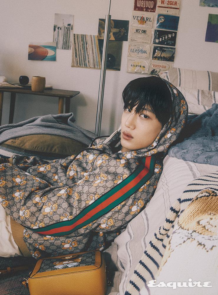Kai x Gucci GG 수프림 저지 스웨트셔츠, 화이트 코튼 쇼츠, 침대 위에 올려진 Kai x Gucci 스트라이프 니트, Kai x Gucci 스몰 숄더백 모두 구찌.