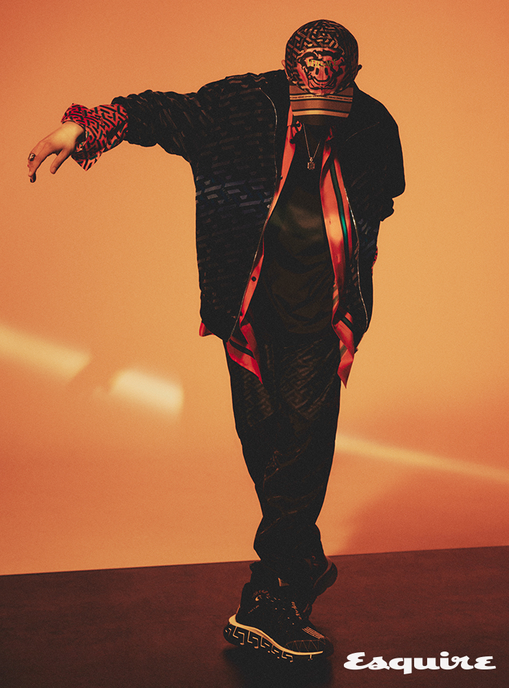 블랙 그래픽 프린트 블루종 재킷, 레드 그래픽 메두사 프린트 셔츠, 블랙 그래픽 프린트 팬츠, 블랙 스니커즈, 메두사 프린트 볼캡, 네크리스 모두 베르사체.