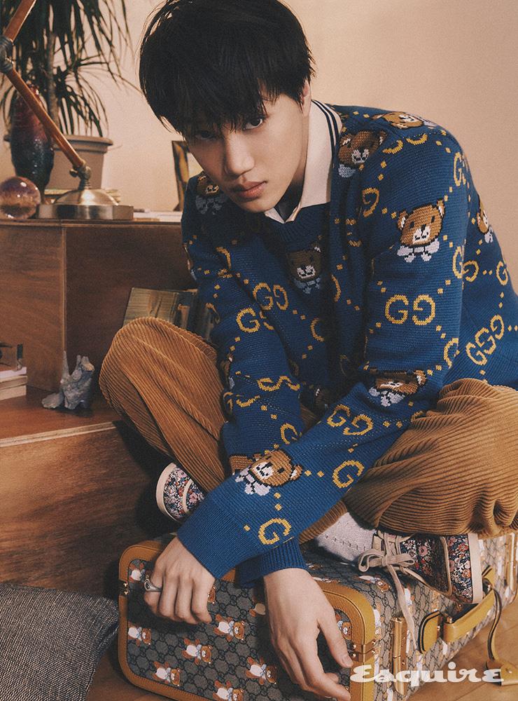 Kai x Gucci 블루 스웨터, 코튼 폴로, 레더 패치 디테일의 코듀로이 팬츠, 플라워 프린트 모카신, Kai x Gucci 슈트 케이스, 화이트 삭스, 링 모두 구찌.
